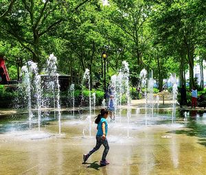 Boy playing in water fountain against trees