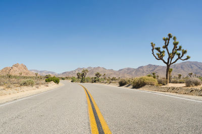 Road amidst desert against clear blue sky