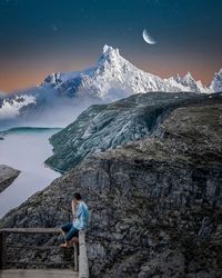 Man sitting on railing against mountains during winter