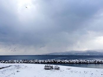 Scenic view of snow covered beach and sea against cloudy sky