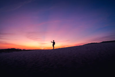 Silhouette man standing on shore against sky during sunset