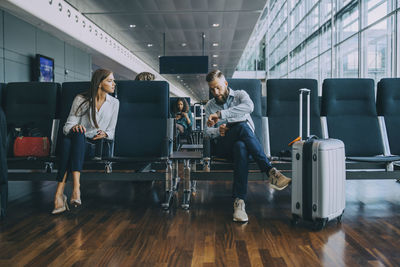 Businessman telling time to businesswoman waiting in airport departure area