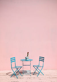 Empty blue chairs and table against wall on sunny day