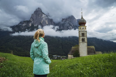 Rear view of woman standing by building against sky