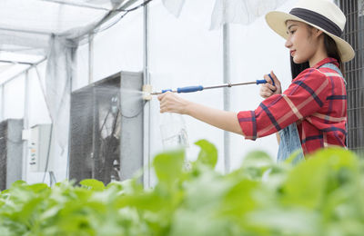 Side view of woman wearing hat watering plants at farm