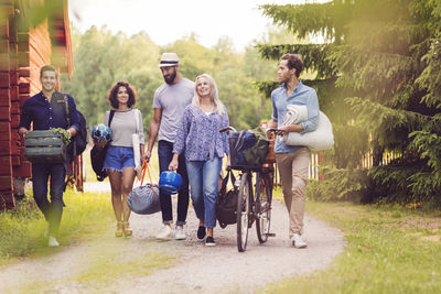 Happy friends with bicycle and luggage walking on pathway by cottage