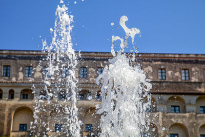 Fountain by building against clear blue sky during winter