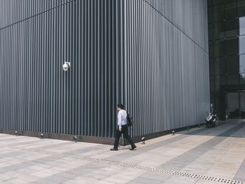 Rear view of man walking on footpath by building