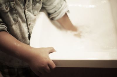 Midsection of boy standing by sink in bathroom