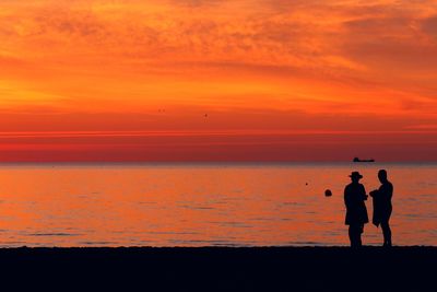 Silhouette people standing on beach against sky during sunset