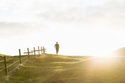 Distant view of man jogging on grassy field against sky during sunny day