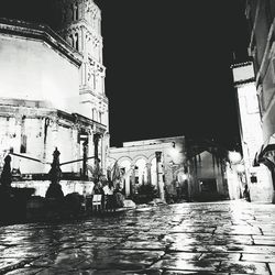 Wet street amidst buildings in city at night