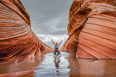 Man standing on rock formation in water against sky