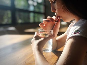 Profile view of girl drinking water while sitting at table