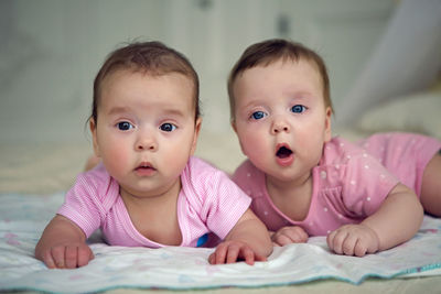 Two sisters twins baby in pink clothes lying on the bed in a diaper