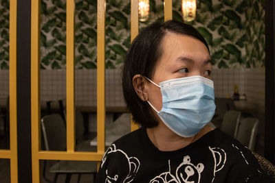 Woman wearing mask looking away standing by gate