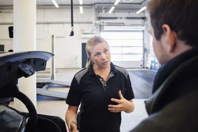 Confident female mechanic discussing with client in auto repair shop