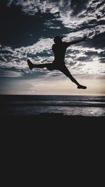 Silhouette man jumping at beach against sky during dusk