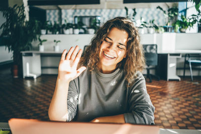 Businesswoman with long loose curly hair talks on video call looking into laptop display 