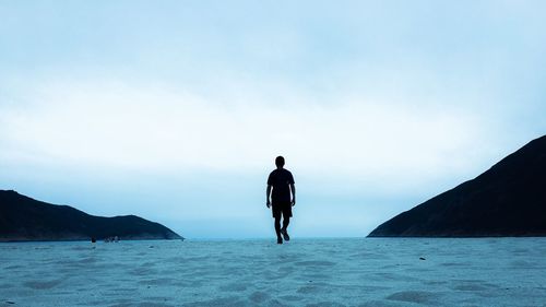 Rear view of man walking on sea shore against clear sky