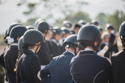 Group of anonymous jockeys in helmets standing in paddock on sunny day in equine club