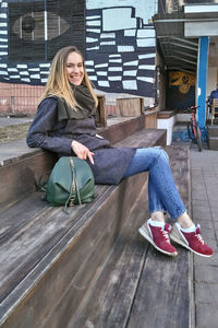 A young woman sits on a wooden step and smiles looking into the camera