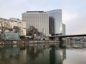 Buildings by river against sky in city