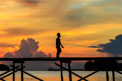 Silhouette man walking on pier over sea against sky during sunset