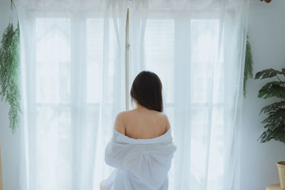 Rear view of woman standing by window at home