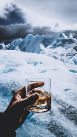 Hand holding ice cream cone against snowcapped mountain
