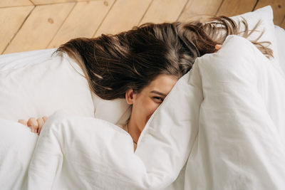 Young cheerful playful woman hides her face under the covers.