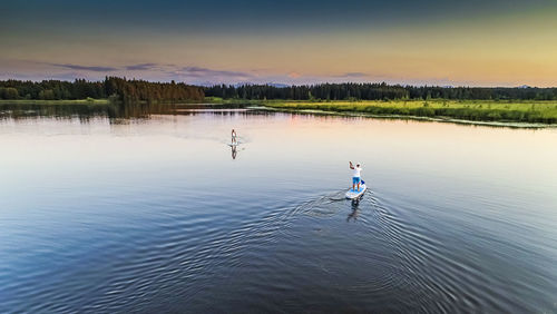 High angle view of friends paddleboarding in lake during sunset