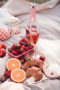 Glass of rose wine with strawberry and fruits and croissants on wooden tray outdoors closeup.