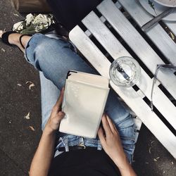 Low section of woman sitting at sidewalk cafe while reading novel