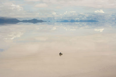 Vehicle with reflection of clouds and mountains at salar de uyuni