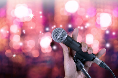 Close-up of cropped hand holding microphone against illuminated lights