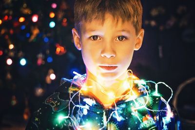 Close-up portrait of boy with illuminated christmas lights at night