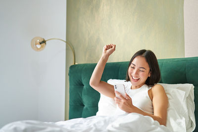 Portrait of young woman using mobile phone while lying on bed at home