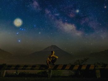 Man sitting on crash barrier against sky at night