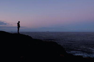 Silhouette of people standing on beach at sunset