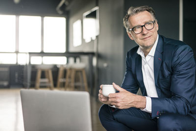 Smiling mature businessman with cup of coffee thinking