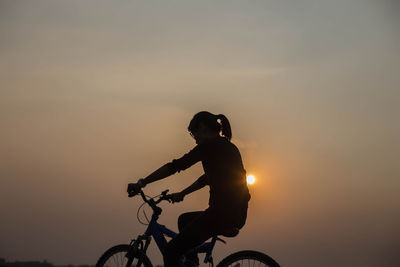 Silhouette woman riding bicycle against sky during sunset