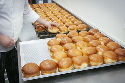 Midsection of man arranging sweet buns on tray in kitchen