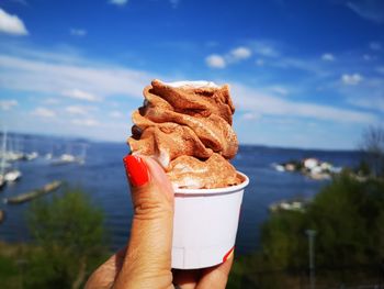 Close-up of hand holding ice cream cone against sky