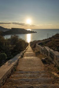 Footpath by sea against sky during sunset