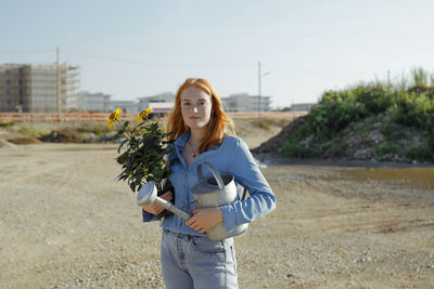 Confident woman holding potted plant and watering can at construction site