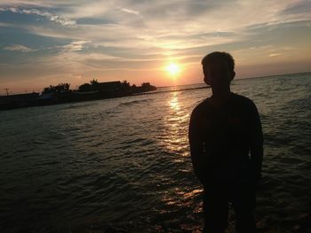 Rear view of silhouette man standing at beach during sunset