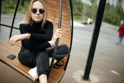 Stylish young blonde is sitting in a round hanging chair outdoor. model sits in a chair and relaxes