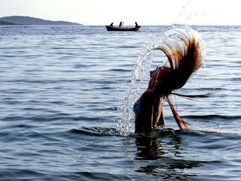 Woman splashing water with hair in sea against sky