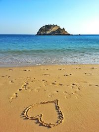 Heart shape drawn at beach against clear sky